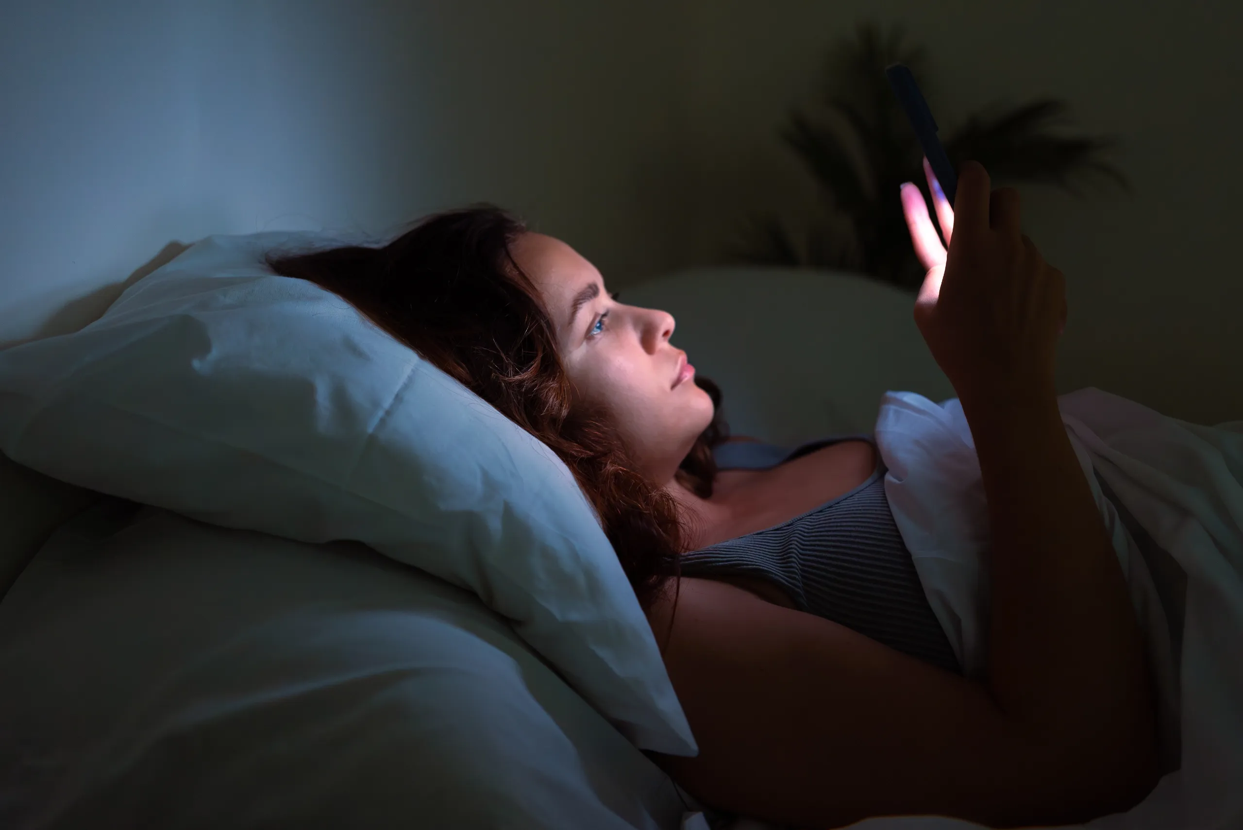 Mujer despierta de noche en la cama usando el móvil necesita tratamiento psicológico para el insomnio