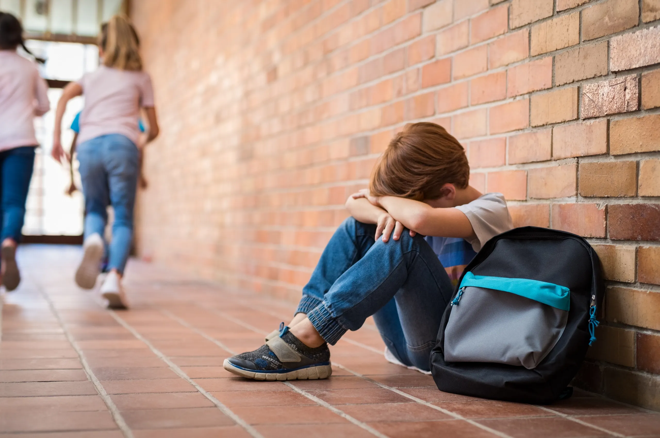 Niño solo sentado en el suelo después de sufrir bullying o acoso escolar en su colegio